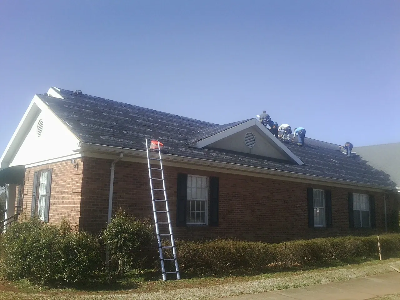 Crew tearing shingles off a brick ranch roof with a ladder set — Metal Roof Repair work by our crew in Panama City