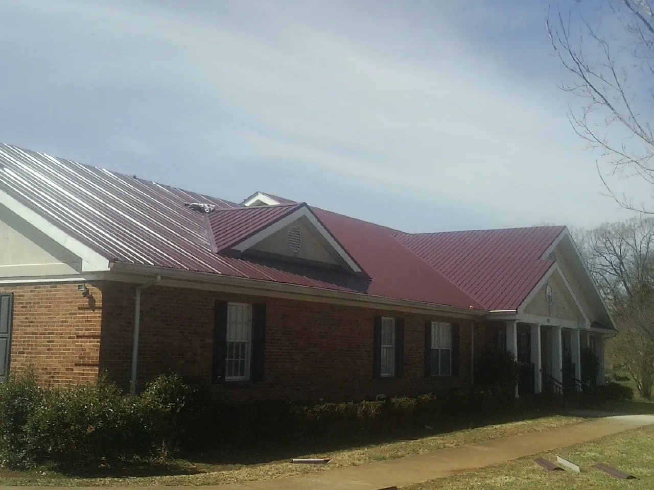 Red metal roof with gabled entries on a long brick building, from a Hail Damage Roof Repair job in Panama City