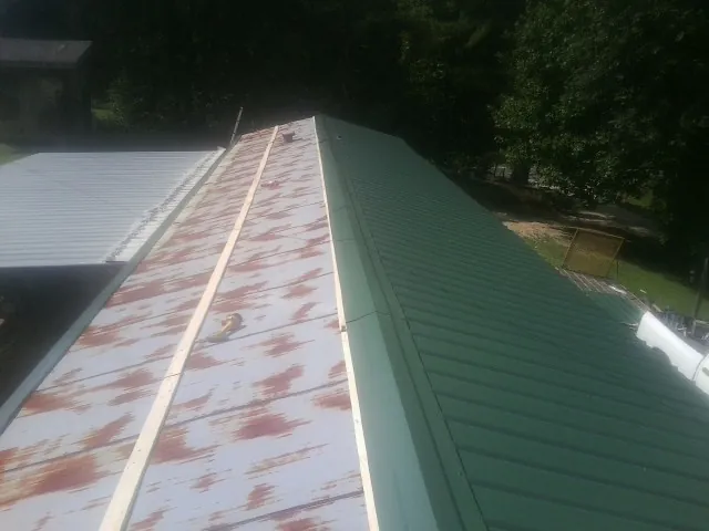 Old rusted panels beside newly installed green metal roofing — Wind Damage Roof Repair by Roofing Brothers in Panama City