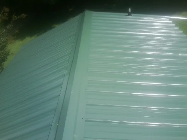 New green metal panels meeting at the ridge of a roof — Flat Roof Repair work by our crew in Panama City