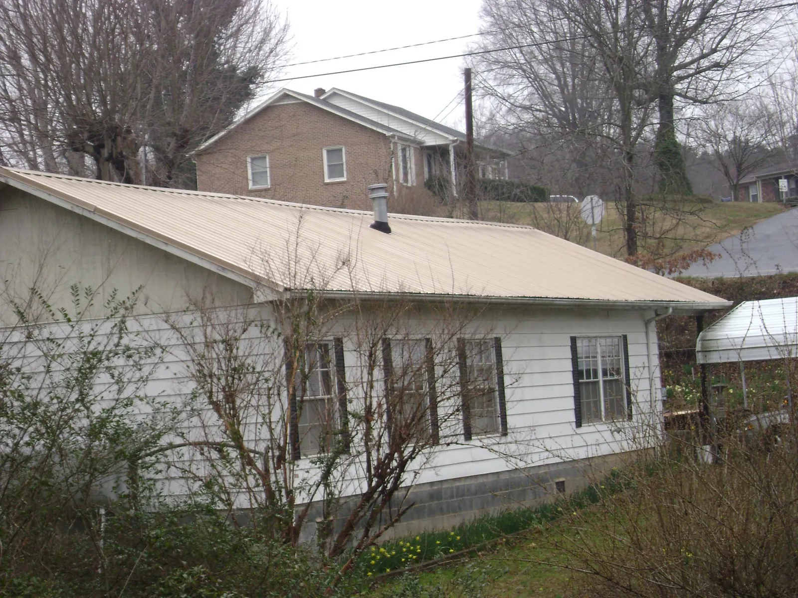 Tan metal roof on a white sided house set into a hillside — Commercial Roofing by Roofing Brothers in Panama City