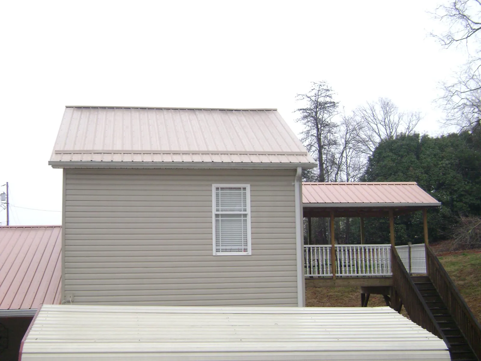 Tan metal roofs on a two story addition and attached porch, from a Roof Replacement job in Panama City